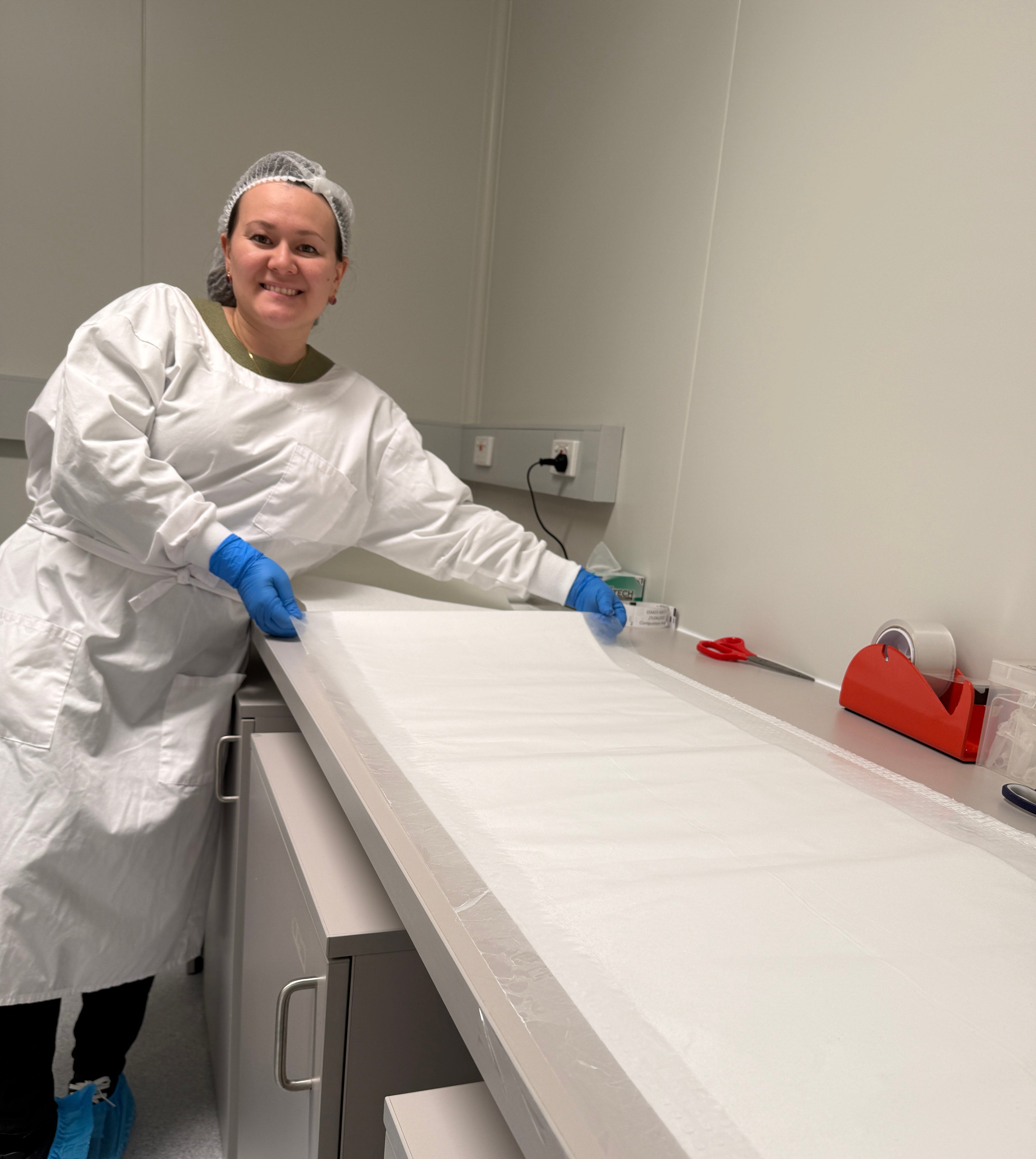Person in a lab setting wearing protective gear, including a white coat and gloves, working on a piece of equipment.